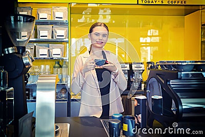 Smiling Coffee shop owner standing behind counter with cup of coffee Stock Photo